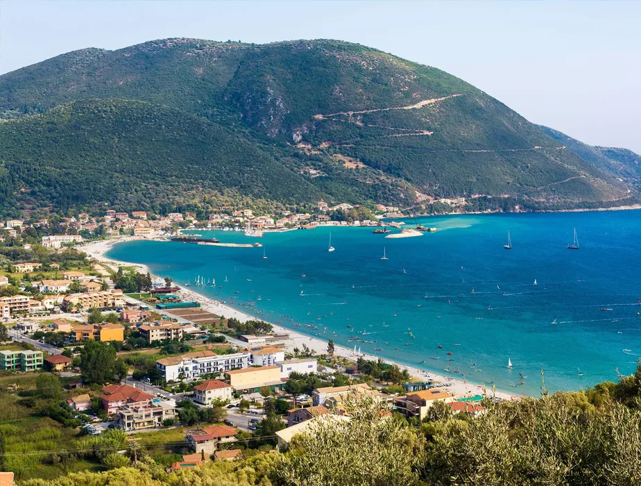 Beach and coastal town with turquoise water, sailboats, and green hills in the background for car rental vacations.