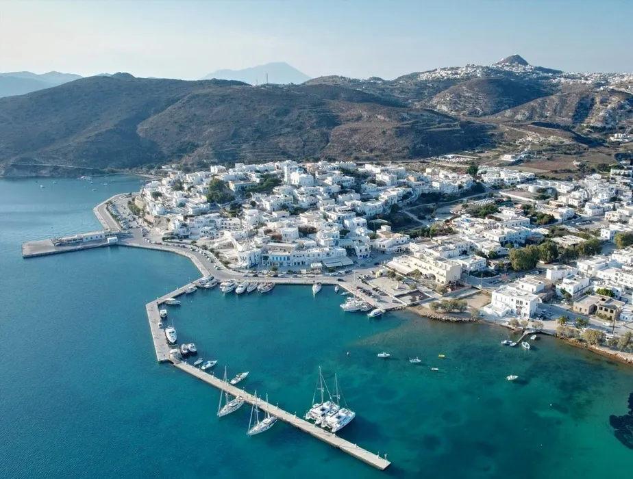 Mykonos harbor with white buildings and boats along the waterfront under clear skies.