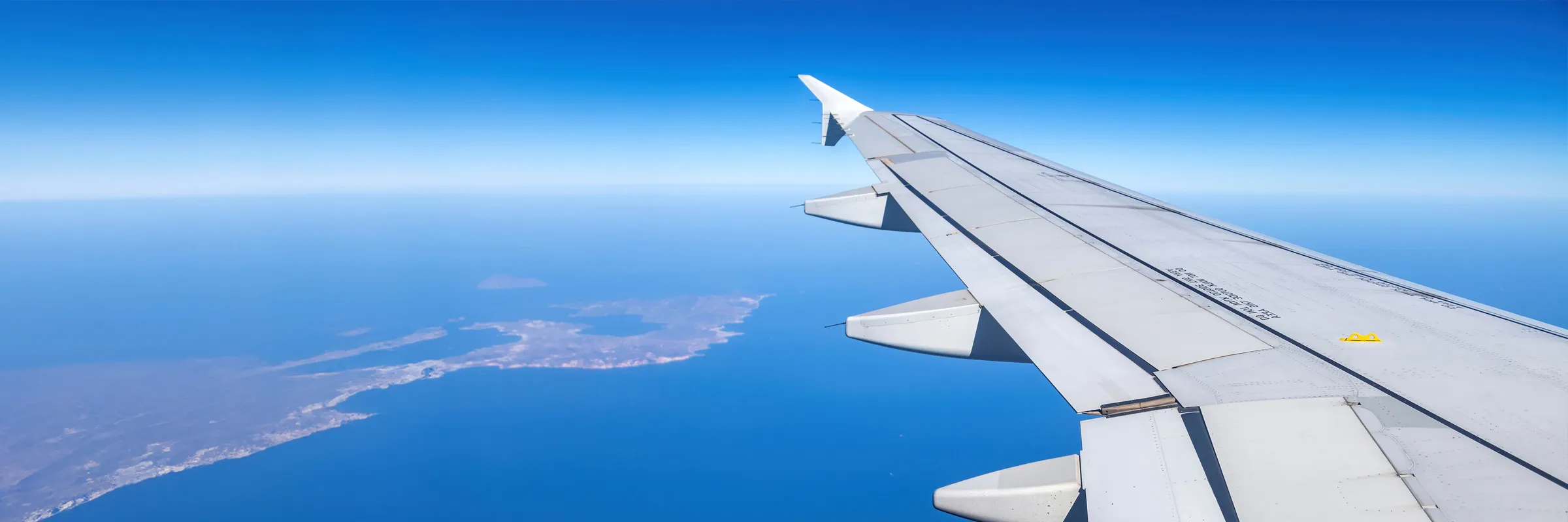 Airplane wing over blue sea and land, suggesting travel and car rental possibilities at destination.
