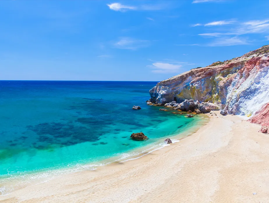 Secluded sandy beach with clear turquoise water and colorful rocky cliffs on a sunny day.