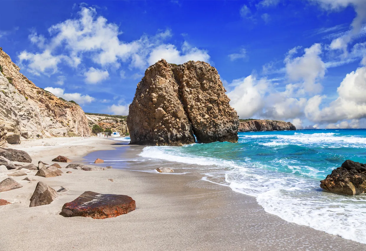 Milos island beach with large rock formations and waves under a blue sky for summer car rental.