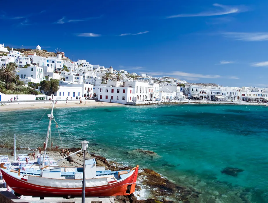 Mykonos Strand mit traditionellen weißen Häusern und rotem Boot am türkisfarbenen Wasser für Autovermietung.