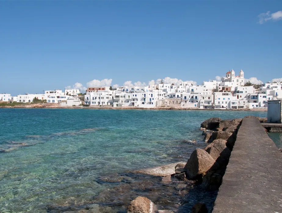Seaside view of Naoussa in Paros with white buildings along the coast and clear blue water.
