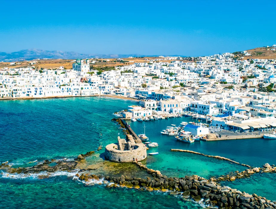 Mykonos harbor with traditional white buildings and boats in the clear blue sea view.