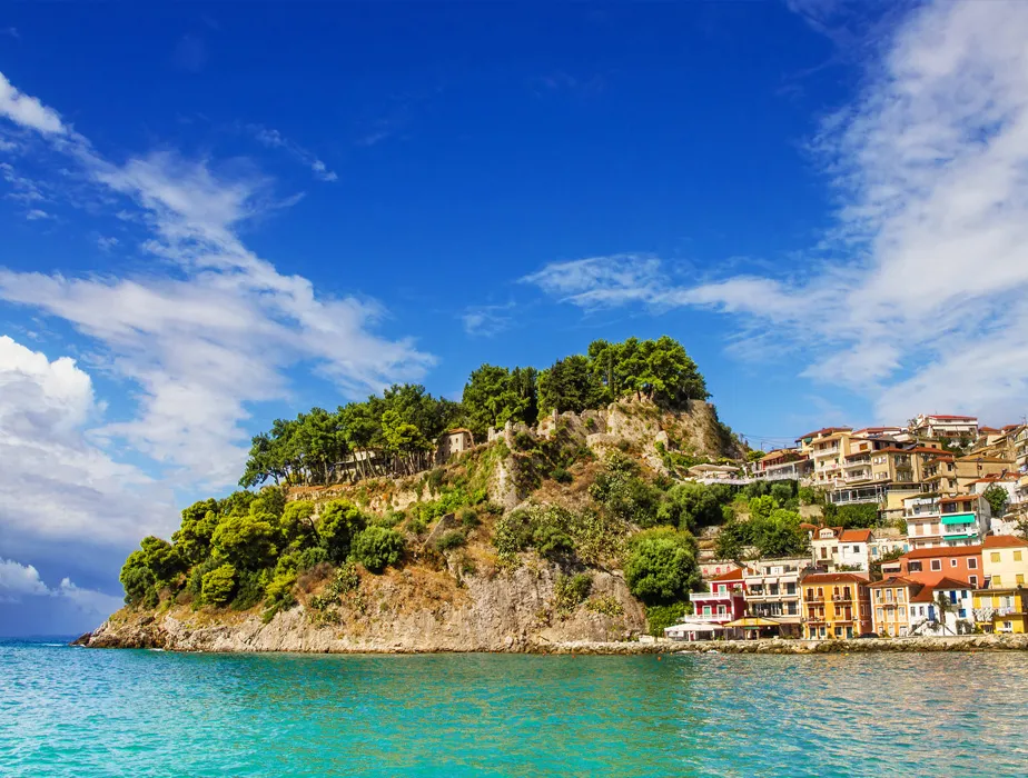 Parga coastline with colorful houses and green trees on a sunny day by the sea.