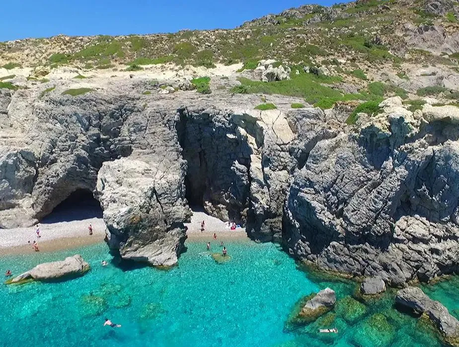 Secluded rocky beach with crystal clear turquoise water and people swimming and relaxing.