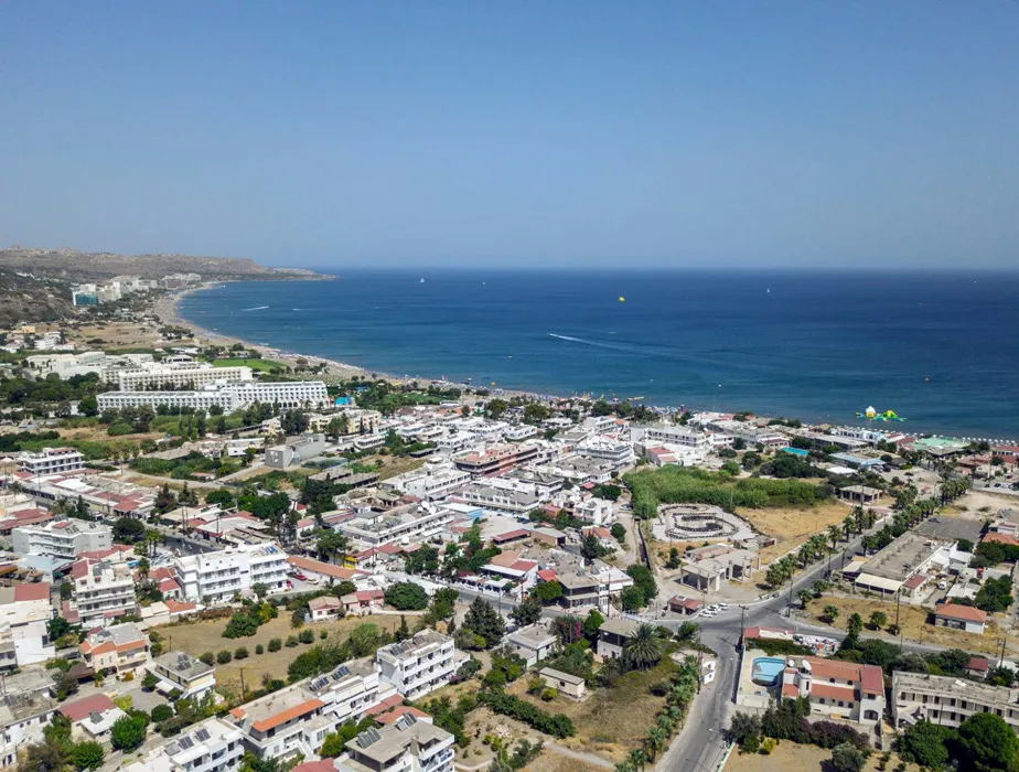 Coastal town with beach and buildings along the shoreline and clear blue sea under a sunny sky.