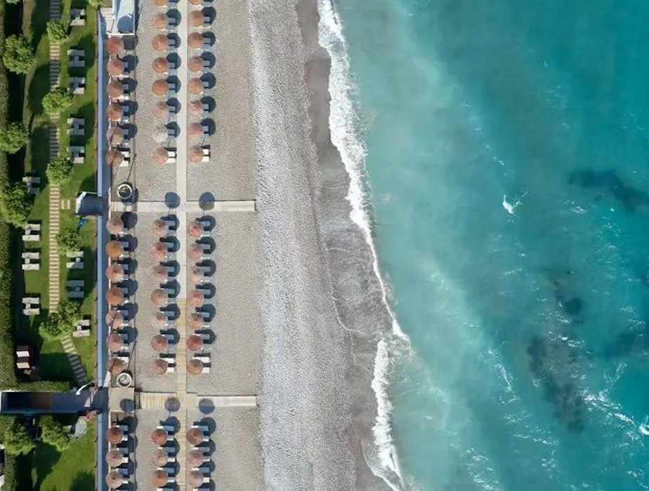 Aerial view of a beach with rows of sun umbrellas and turquoise sea waves at the shore.