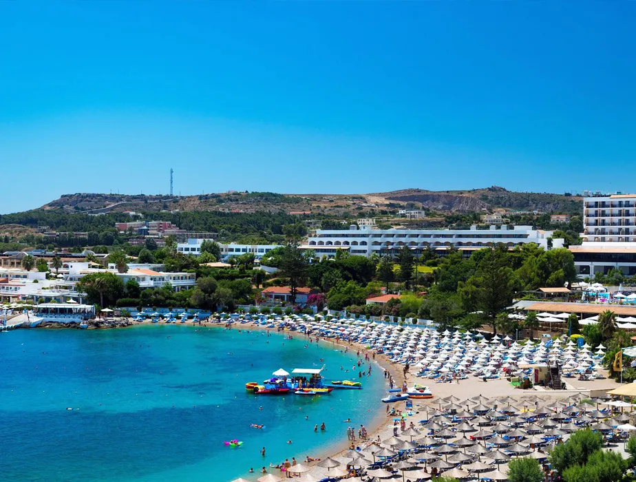 Lindos beach in Rhodes with sunbeds and umbrellas by clear blue water in a popular summer destination.