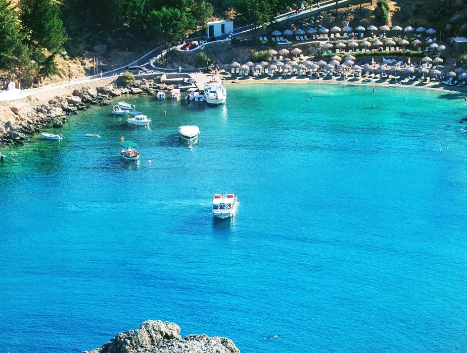 Secluded beach bay with boats anchored on clear blue waters and shaded umbrella seating area.