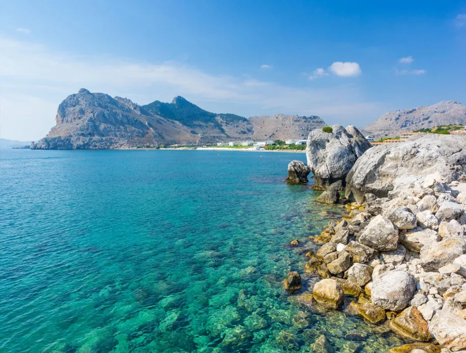 Paesaggio costiero con acqua turchese limpida e costa rocciosa sotto un cielo parzialmente nuvoloso.