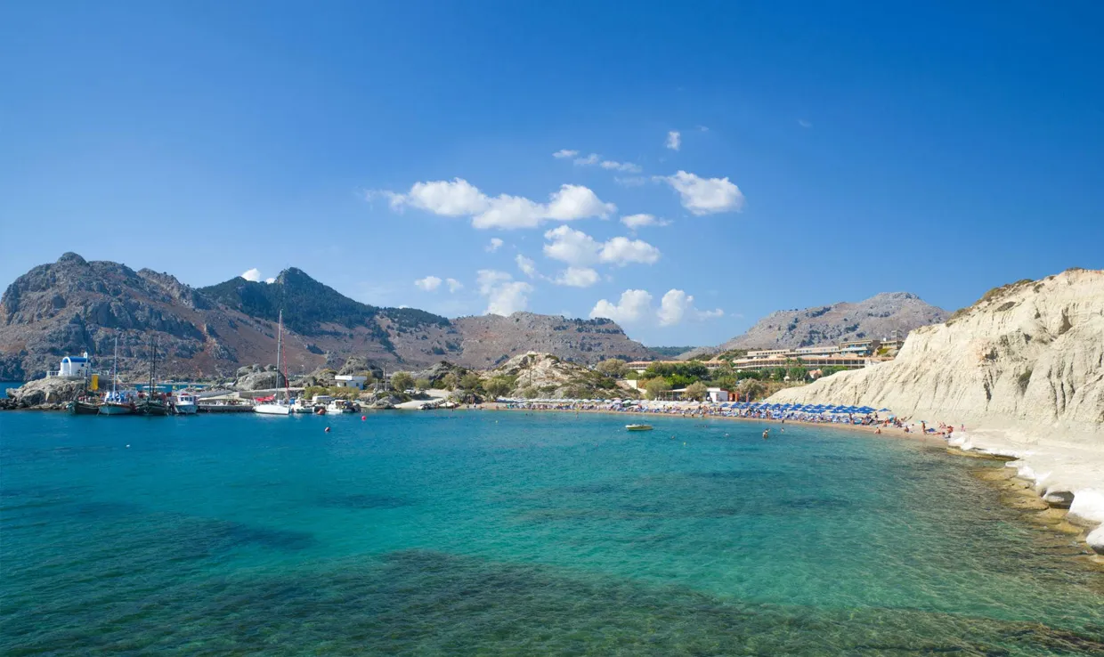 Spiaggia con acqua turchese, barche e colline rocciose sotto un cielo limpido in Grecia.