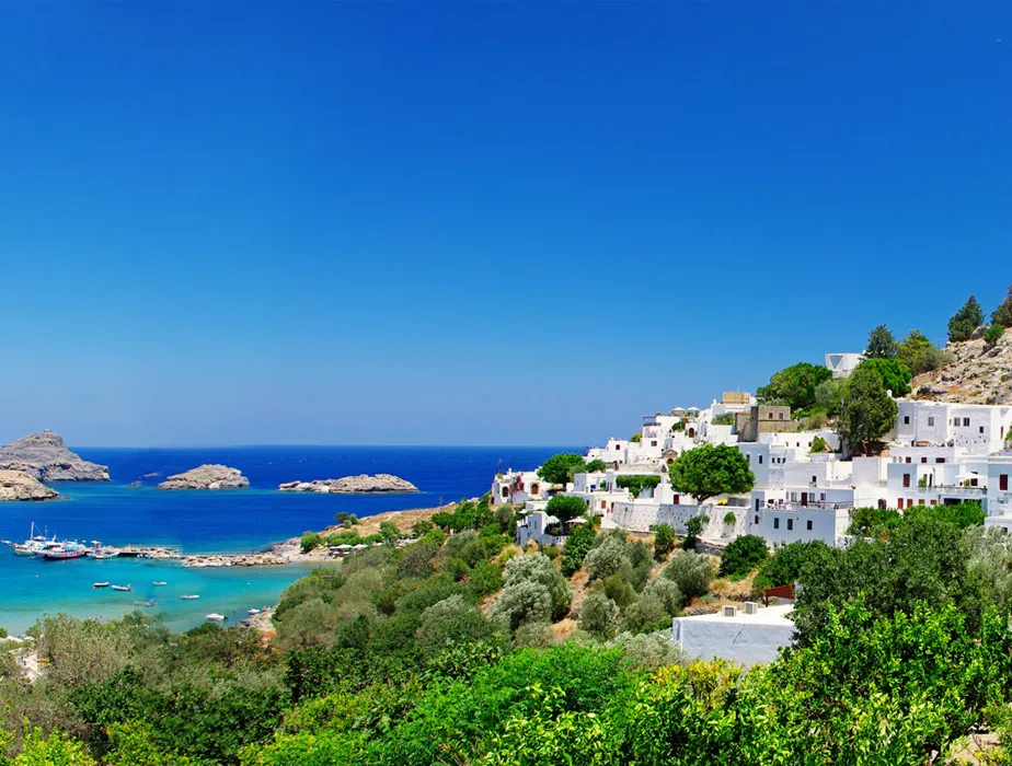 Lindos village on Rhodes island with white houses and turquoise sea under a clear blue sky.
