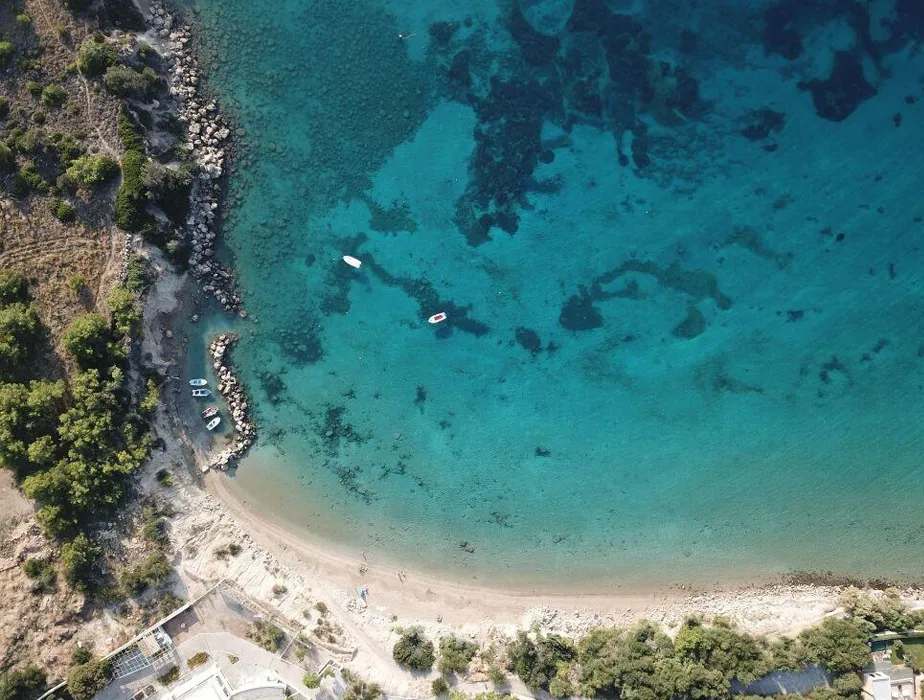 Aerial view of a clear turquoise sea with small boats and a sandy beach for a coastal car rental location.