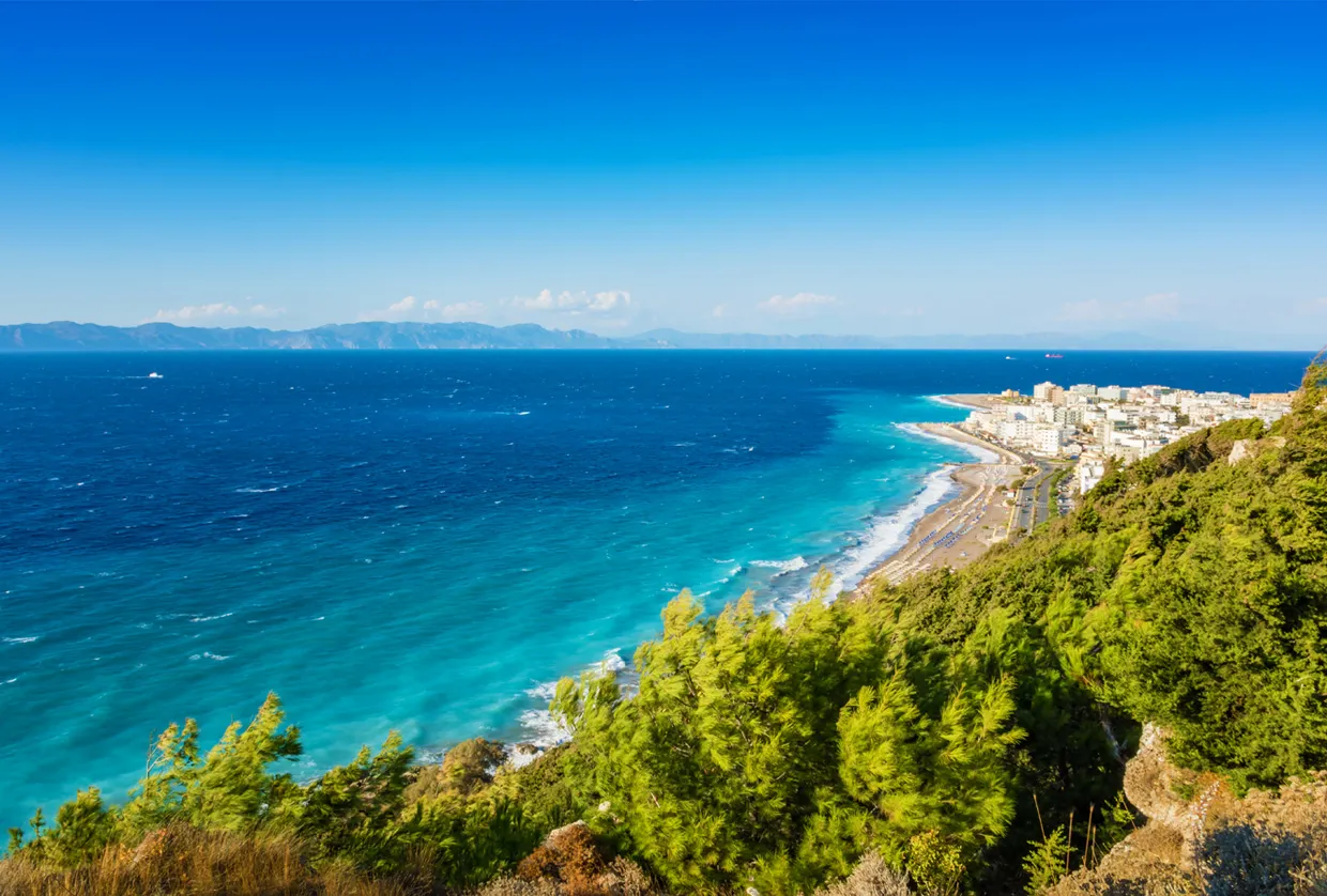 Costa di Rodi con mare azzurro limpido e una città lontana visibile lungo la costa.