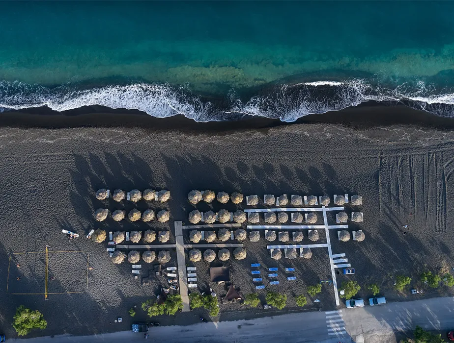 Aerial view of a serene beach with umbrellas, lounge chairs, and calm turquoise waves by the shore.