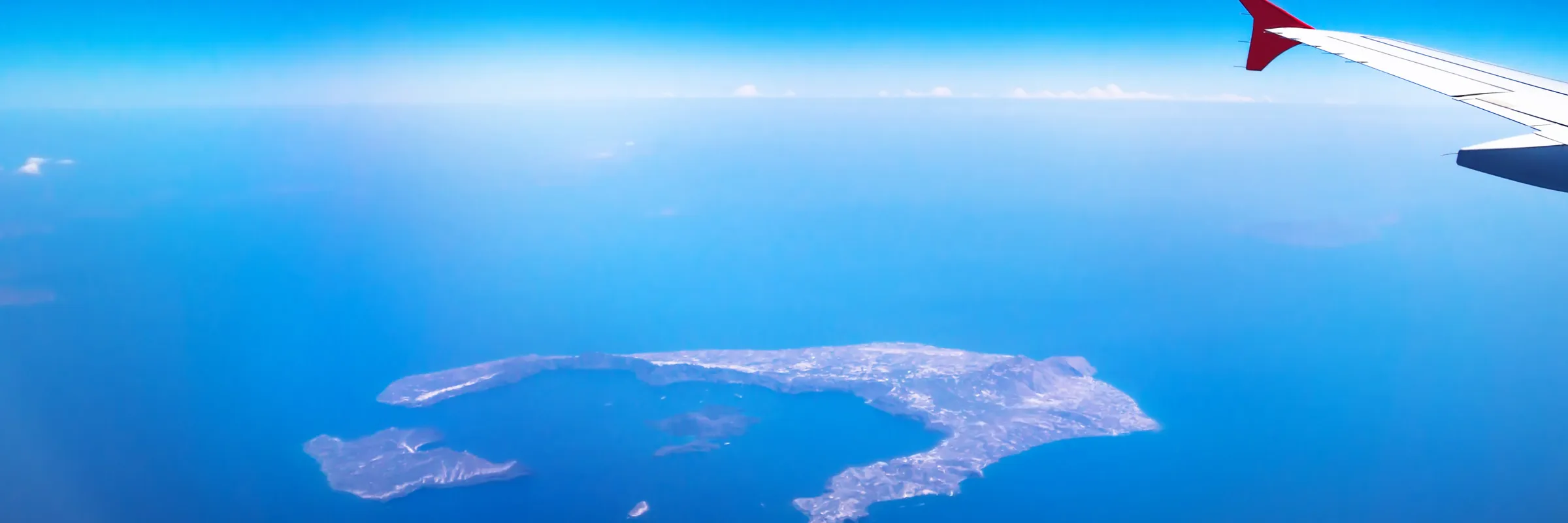 Aerial view of a volcanic island in the sea with a plane wing in the foreground for travel and car rental.