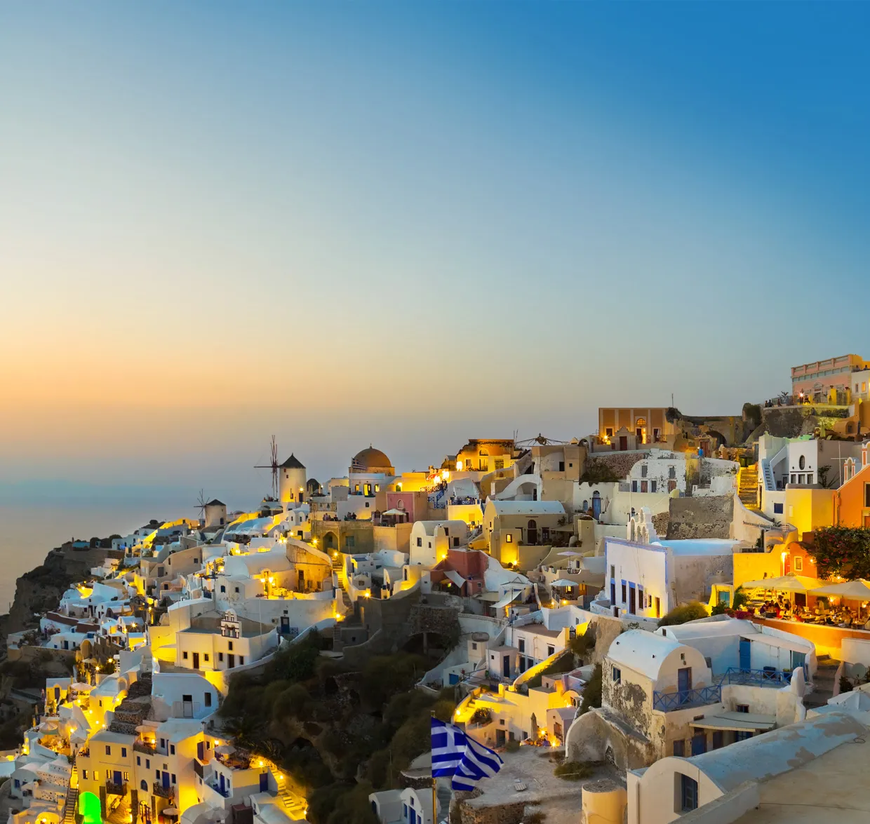 Satul Santorini luminat la amurg cu clădiri albe şi mori de vânt pentru închiriere maşini.