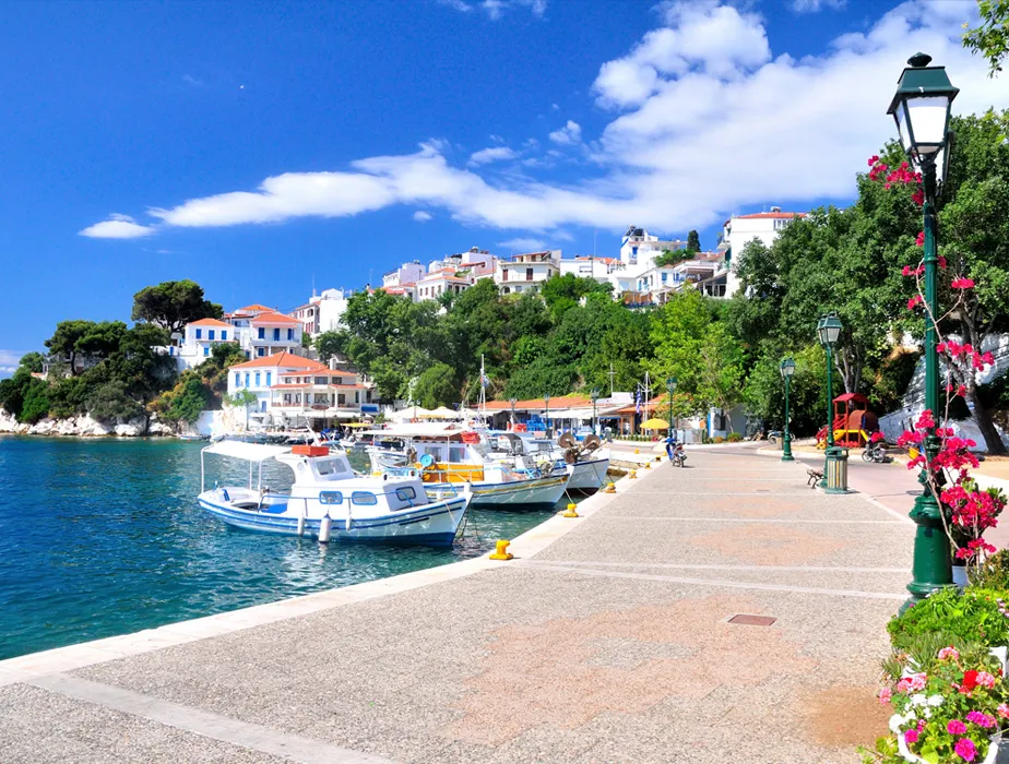 Hafen von Skiathos mit angelegten Booten und Küstendorf unter klarem, sonnigem Himmel.
