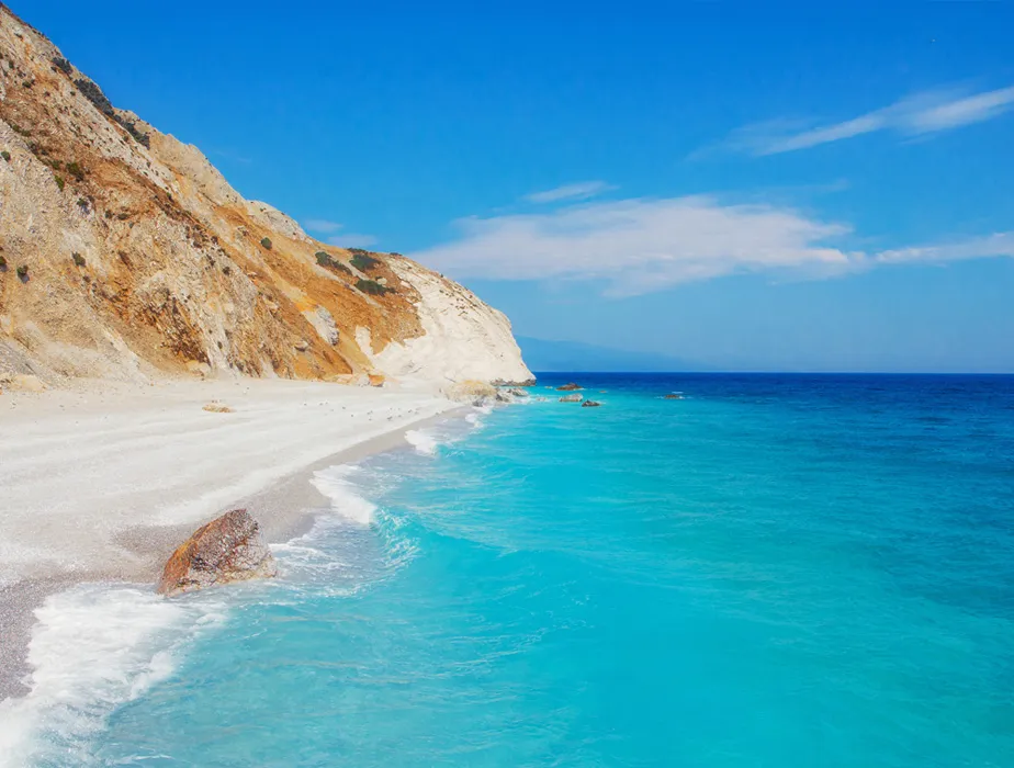 Abgelegener Strand mit klarem türkisfarbenem Wasser und felsigen Klippen unter einem hellblauen Himmel.