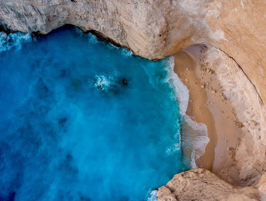 Navagio Beach, Zakynthos, Greece, with clear blue waters and sandy shore enclosed by cliffs.