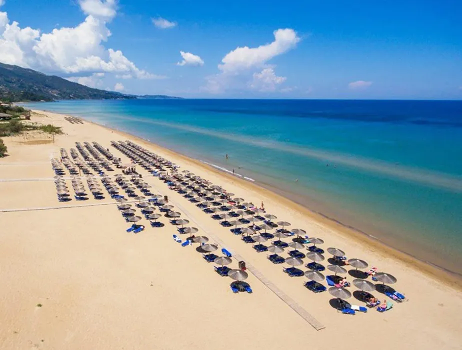 Long sandy beach with rows of umbrellas and sunbeds along a clear turquoise sea shore.