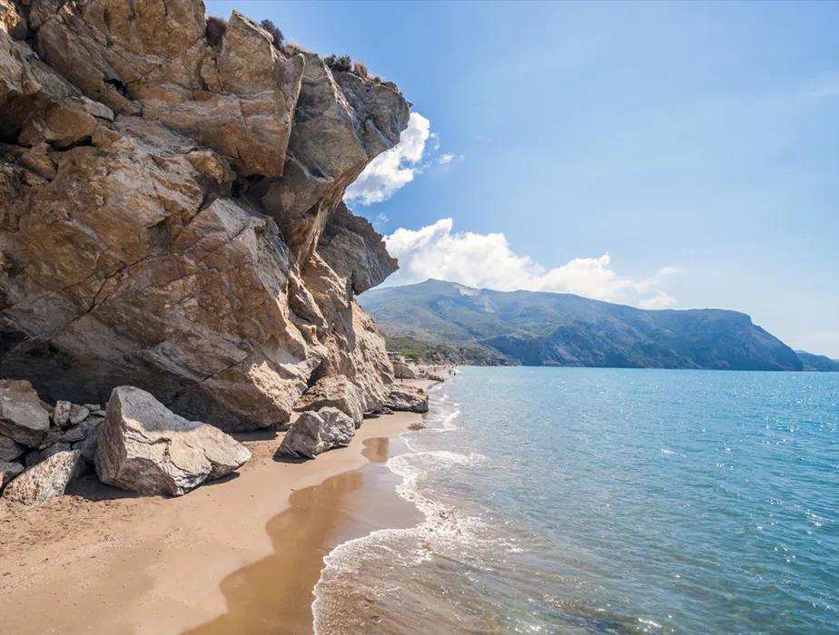 Seaside beach with rugged cliffs and mountains under a clear blue sky.