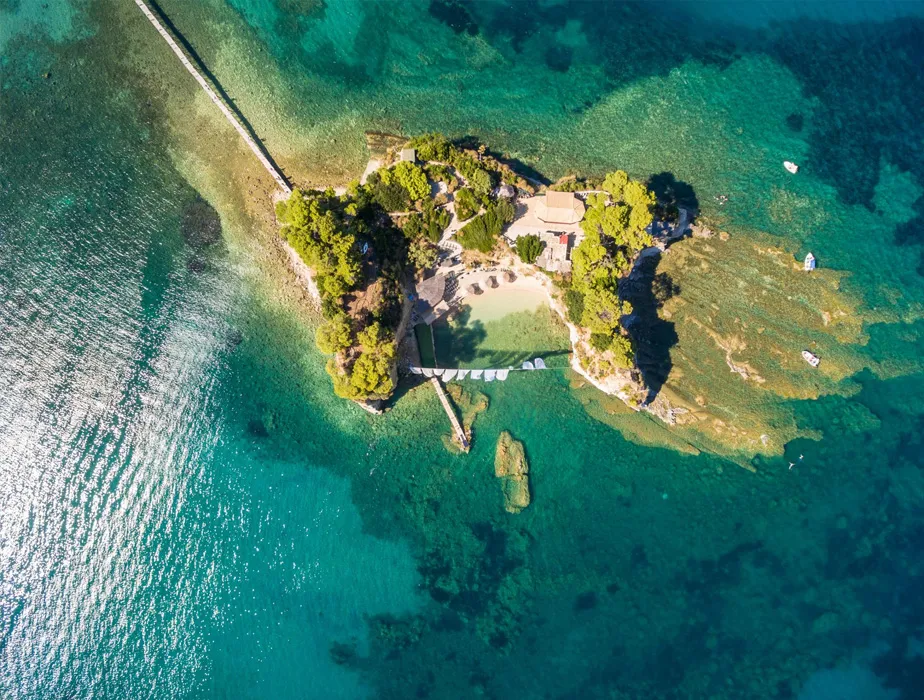 Small private island with turquoise water and beach surrounded by greenery and boats nearby.