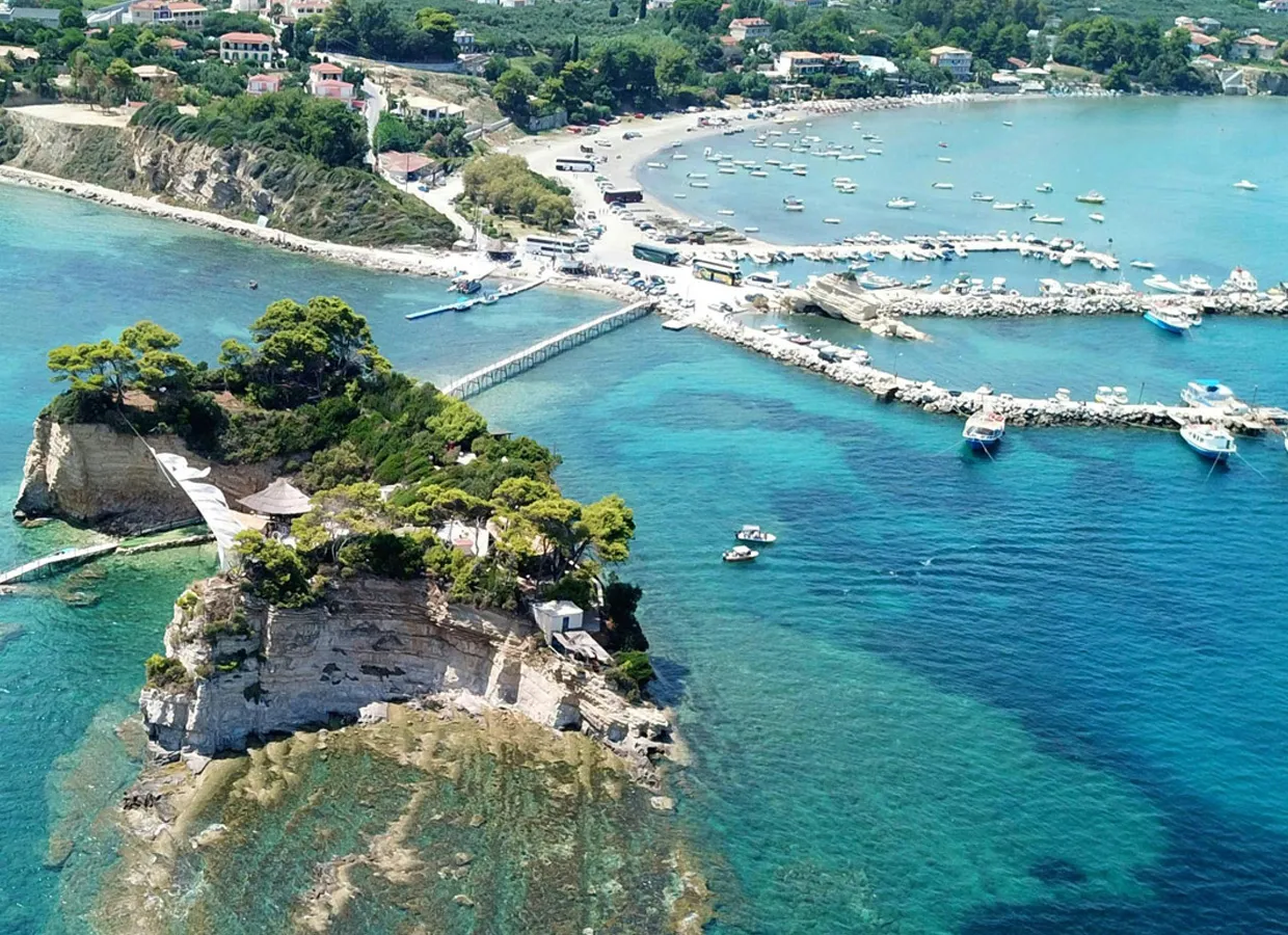 Parga coast view with a small peninsula, turquoise sea, anchored boats, and vacation homes nearby.