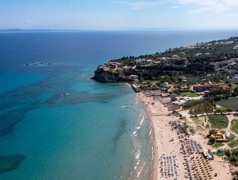 Aerial view of a beachfront resort area with clear blue sea and sandy beach lined with umbrellas for car rental tourists.