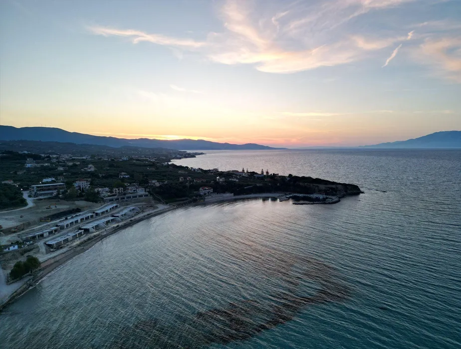 Coastal area at sunset with calm sea and scattered houses near the shore.