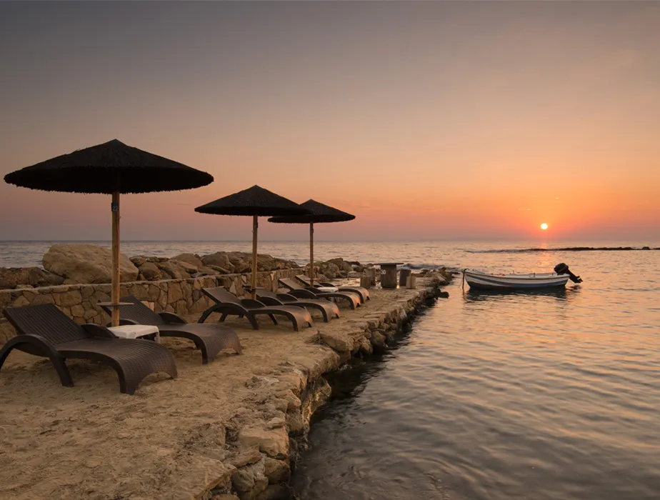 Beachside loungers and umbrellas on a rocky pier by the calm sea during a sunset scene.