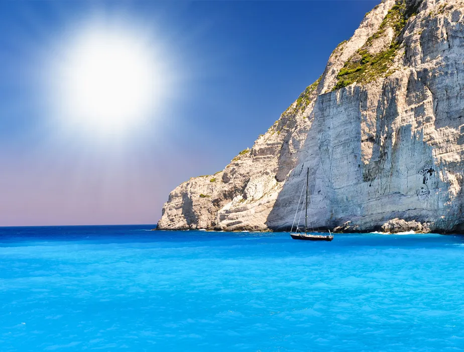 Costa dell'isola di Zacinto con sole splendente, mare blu e una barca a vela vicino a scogliere bianche.