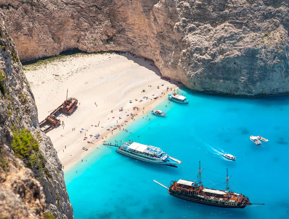 Spiaggia di Navagio a Zante con barche vicino alla riva e un relitto sulla spiaggia di sabbia.