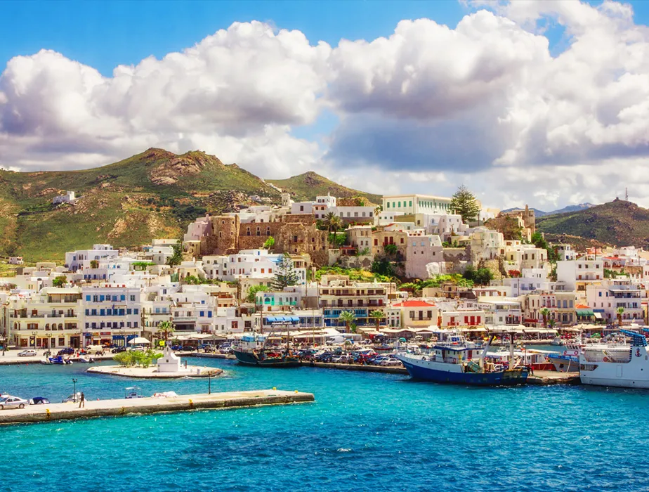 Hafen auf der Insel Naxos mit weißen Gebäuden und Booten unter teilweise bewölktem Himmel.