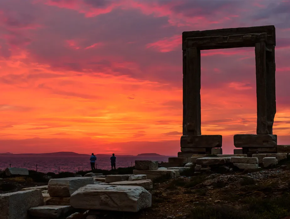Antike Steintor-Ruinen auf Naxos bei Sonnenuntergang mit zwei Personen am Meer.