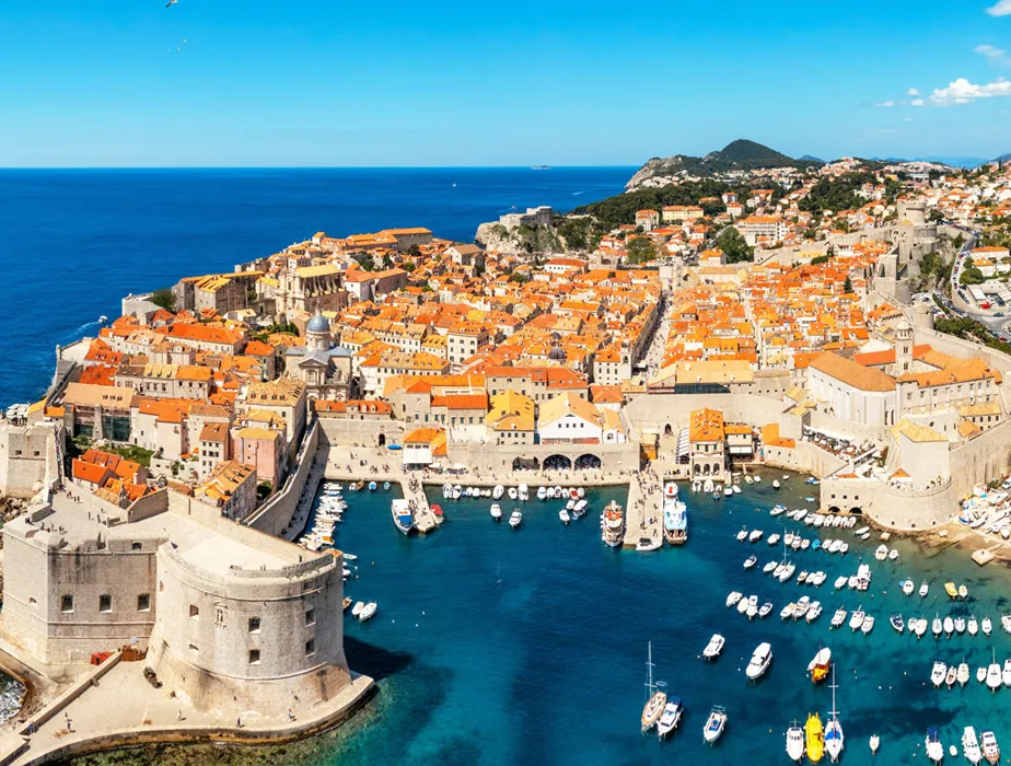 Dubrovnik coastline with historic buildings and boats in the harbor under a clear blue sky.