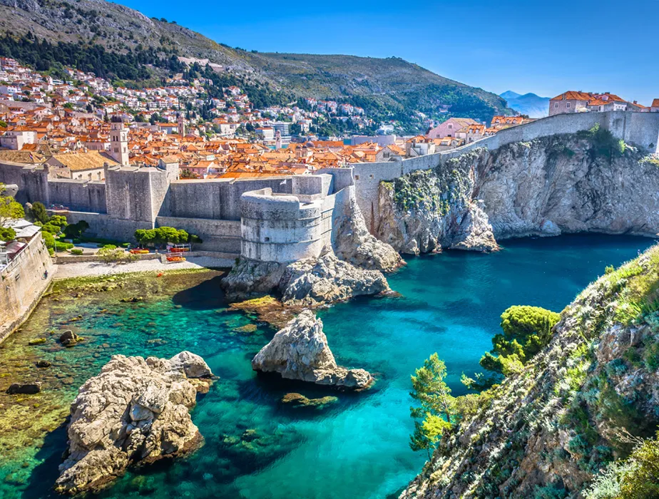 Dubrovnik coastline with ancient stone walls and clear turquoise sea under blue sky.