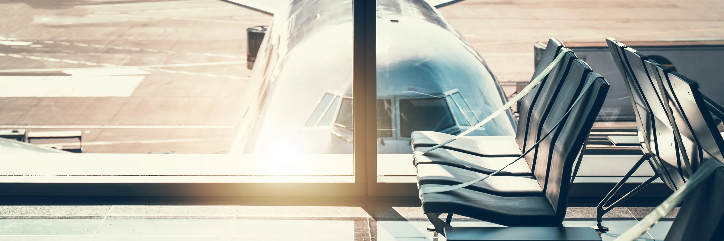 Airport waiting area with empty seats and a large airplane parked outside the window at the terminal.
