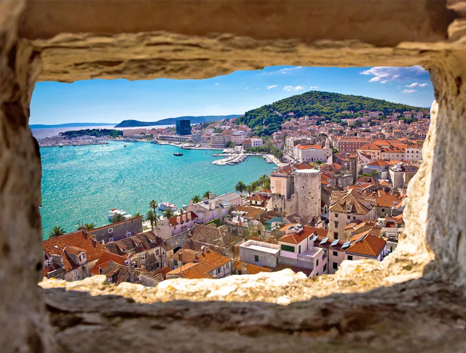 Split view of Split city in Croatia showing the sea, boats, and historic buildings from a stone window frame.