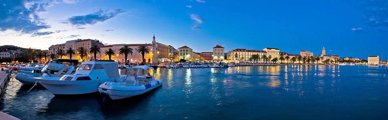 Split split panorama view of Split waterfront at dusk with boats and lit buildings along the shore.
