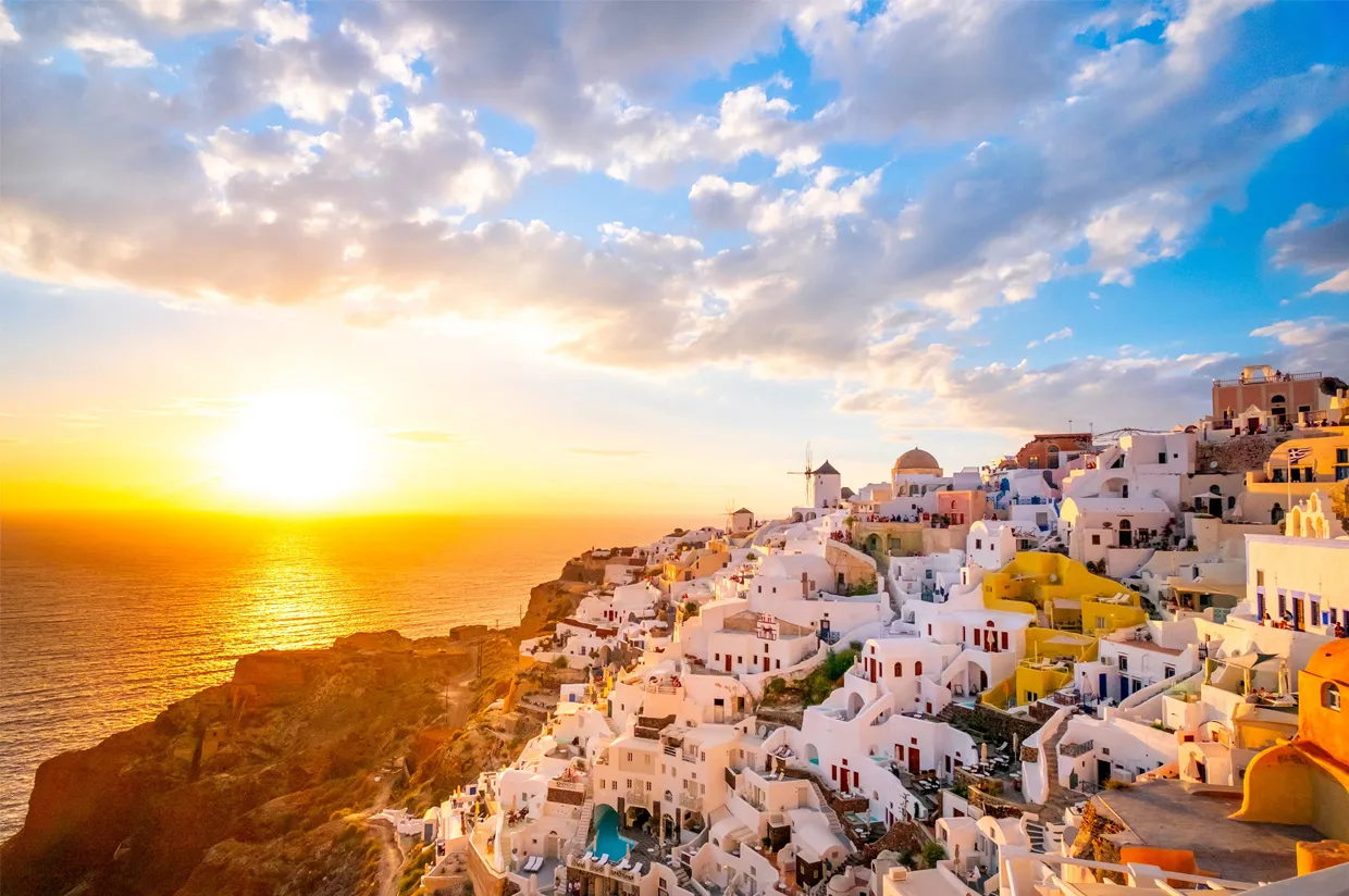 Küstenlinie der Insel Santorini mit weißen Gebäuden und farbigen Akzenten bei Sonnenuntergang über dem Meer.