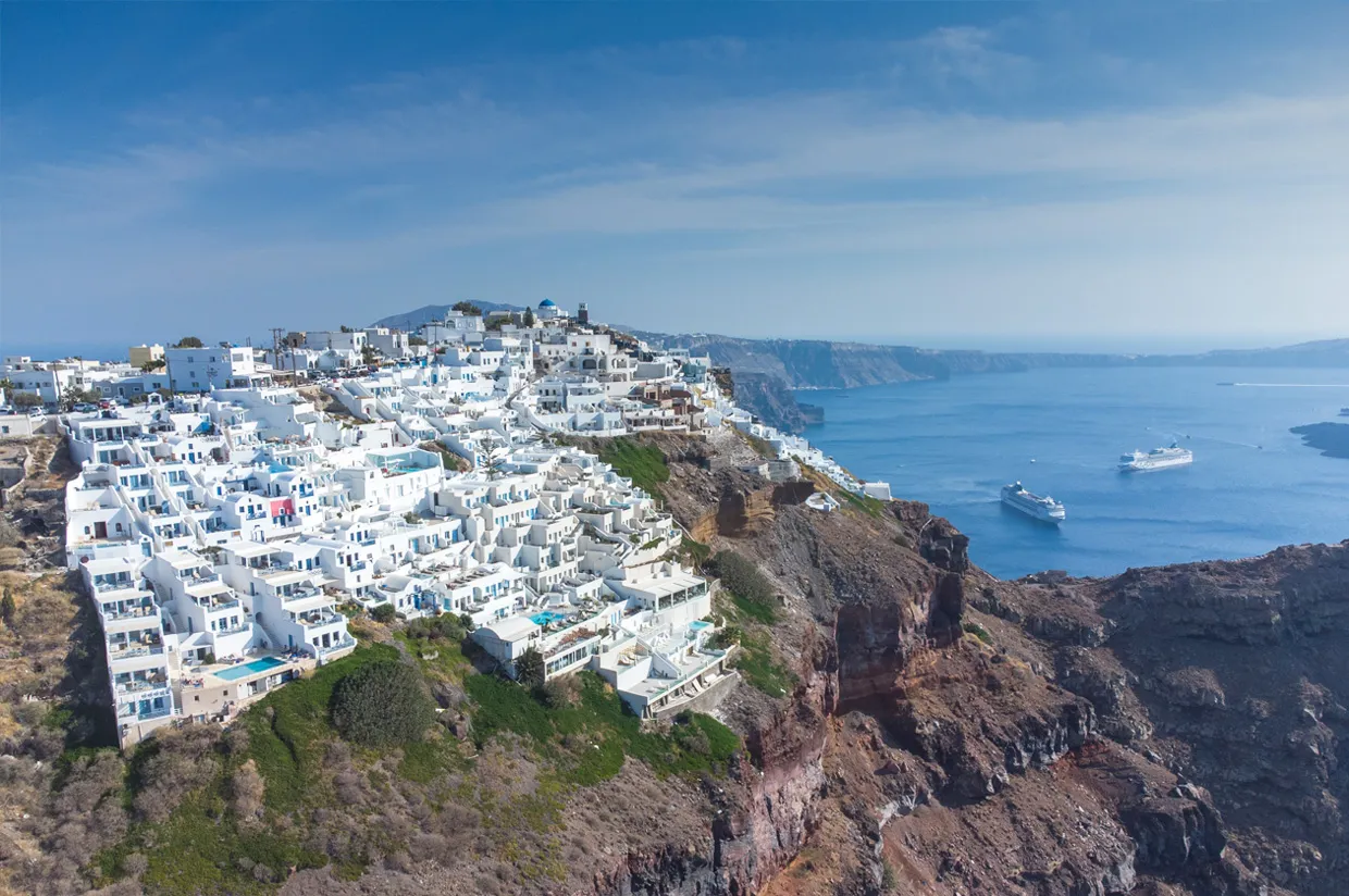 Insel Santorin mit weißen Gebäuden an der Klippe mit Blick auf das Meer und Kreuzfahrtschiffe.