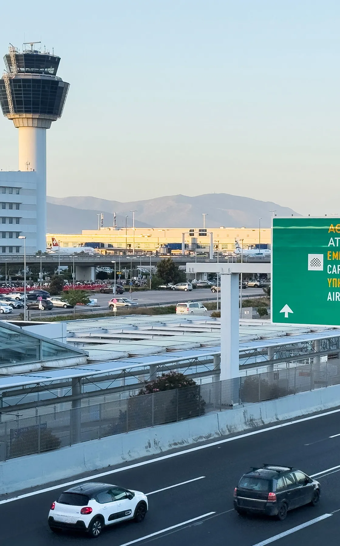 Airport control tower with two cars driving on a highway nearby during daylight.