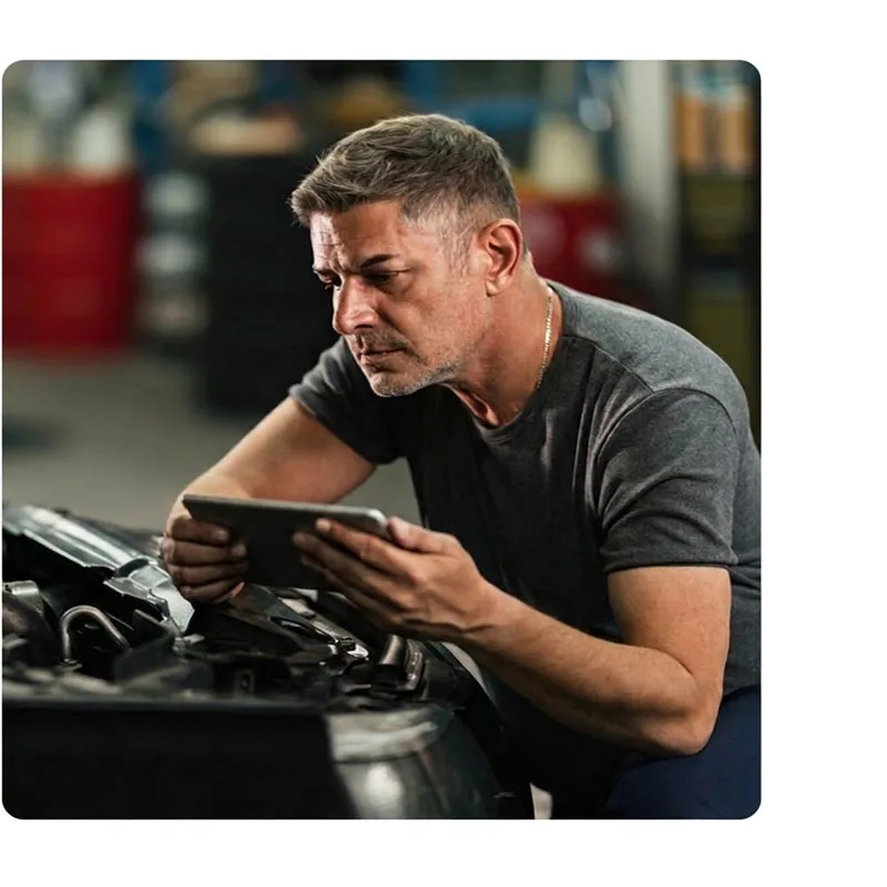 Man using a digital tablet to diagnose or repair a car engine in a professional garage setting.