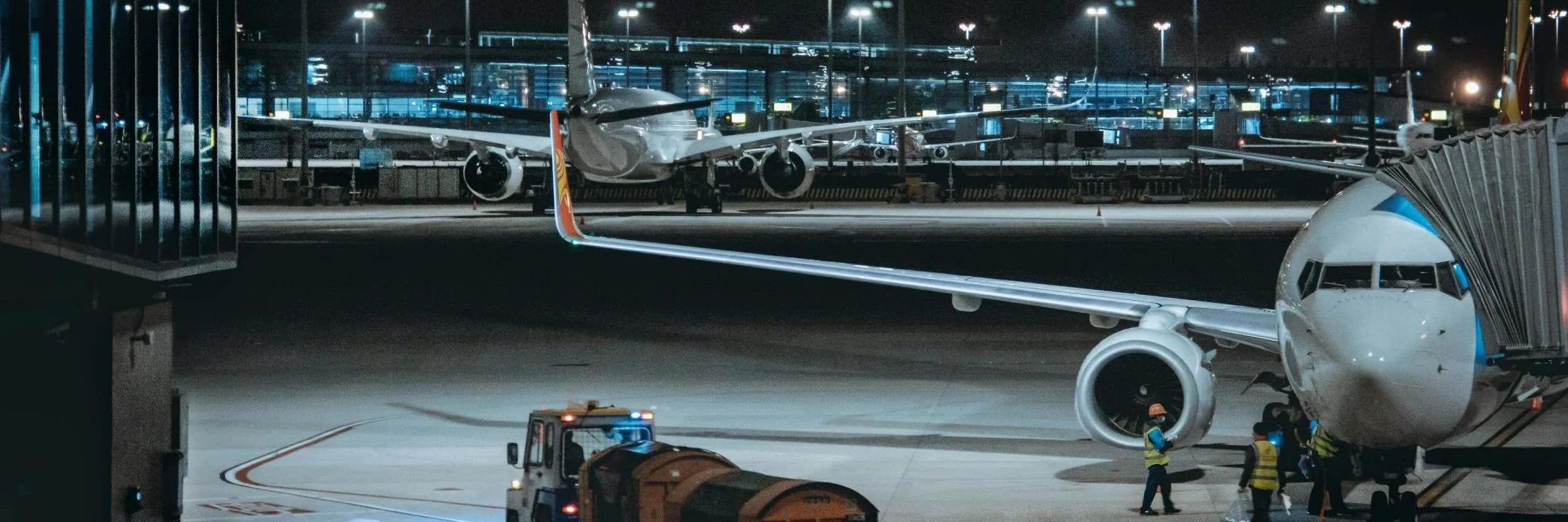 Airport runway at night with airplanes parked and ground crew attending to a plane near the jet bridge.