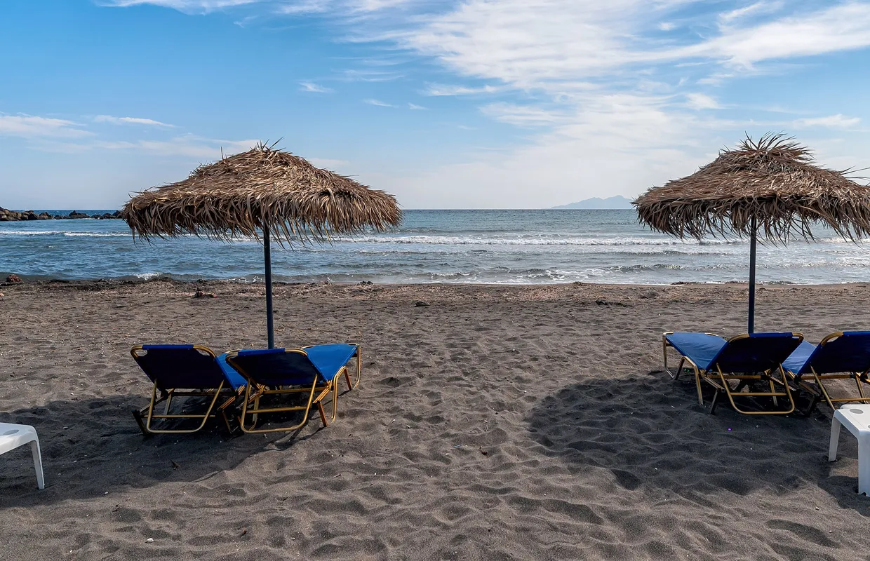 Relaxing beach scene with straw umbrellas and blue sun loungers on dark sand by the sea.