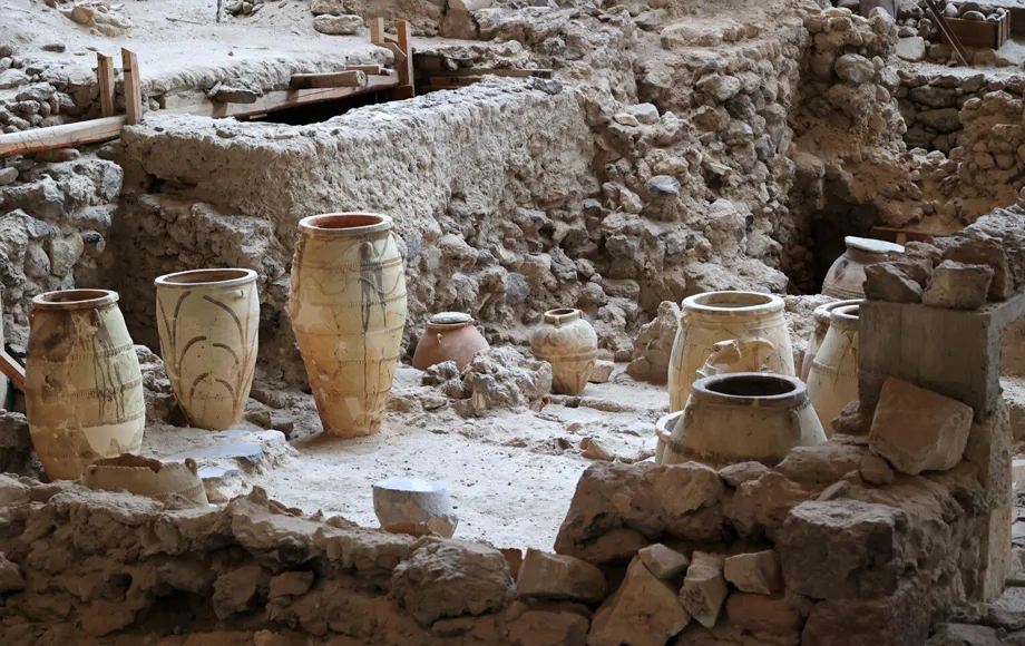Ancient archaeological site with large clay pots and stone ruins in a partially covered area for car rental visitors.