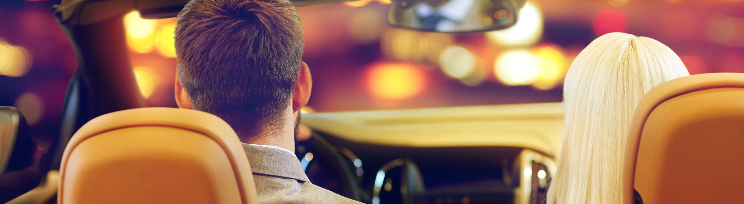 Couple sitting inside a rental car with city lights blurred in the background at night.