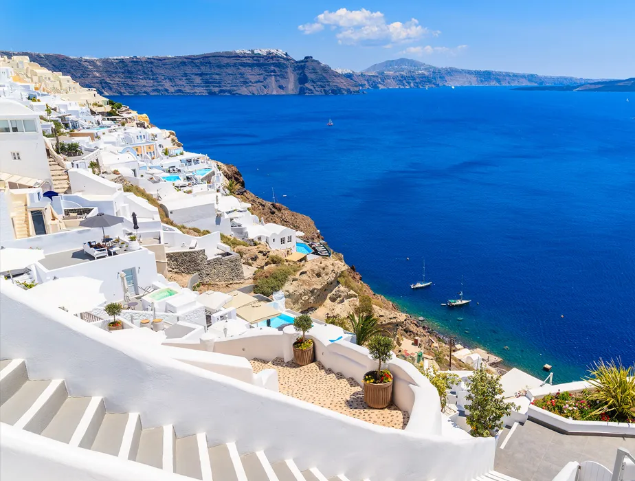 Santorini white buildings on cliffs overlooking the Aegean Sea with boats on clear blue water.